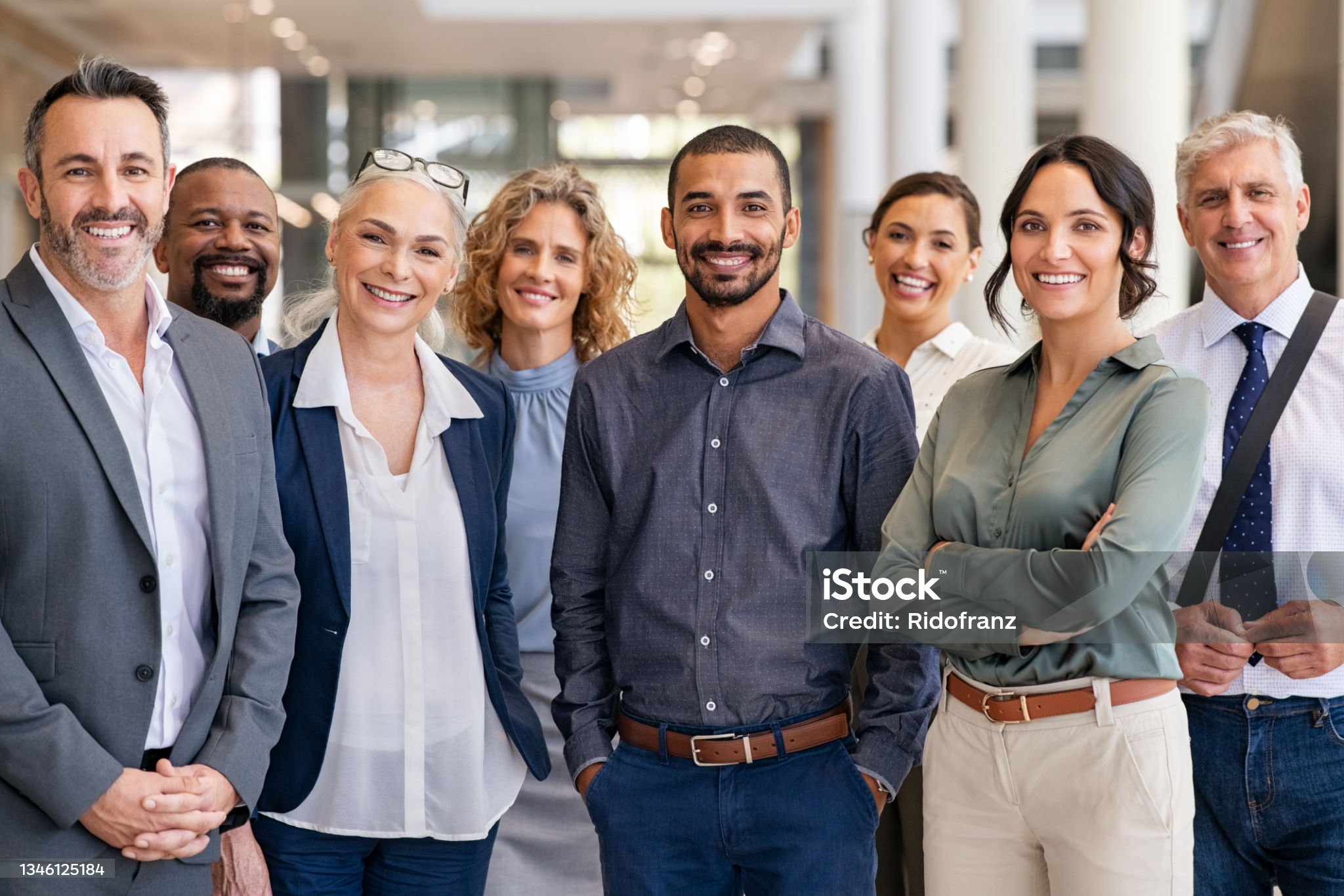 Portrait of successful group of business people at modern office looking at camera. Portrait of happy businessmen and satisfied businesswomen standing as a team. Multiethnic group of people smiling and looking at camera.