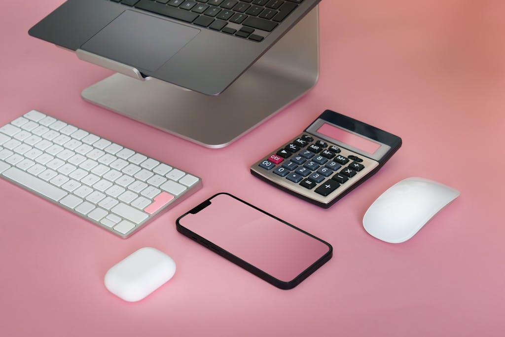 Top view of a minimalist workspace featuring electronic gadgets on a pink background.